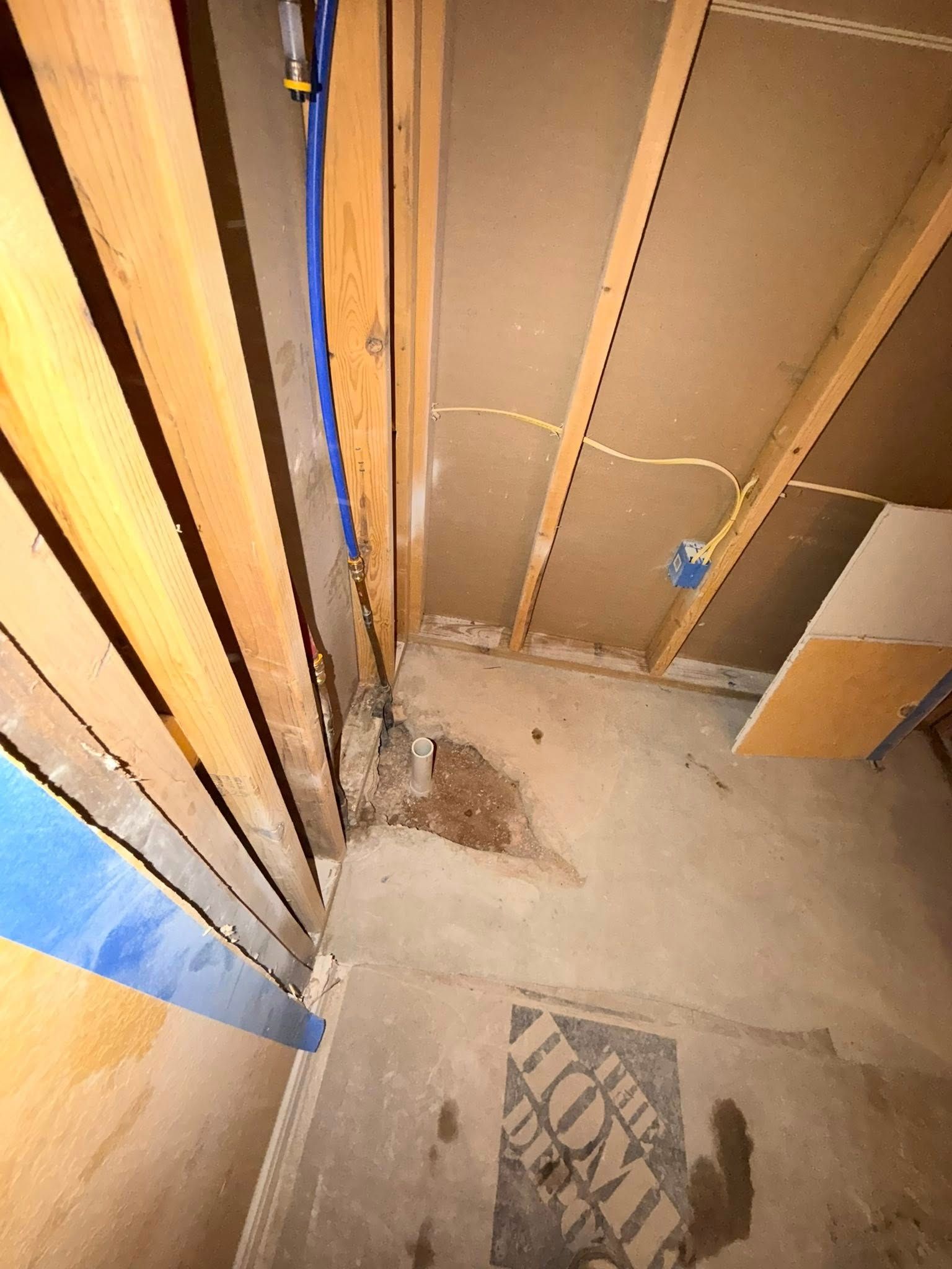 Basement corner with exposed wood framing, concrete floor, and utility lines; possible water damage present.