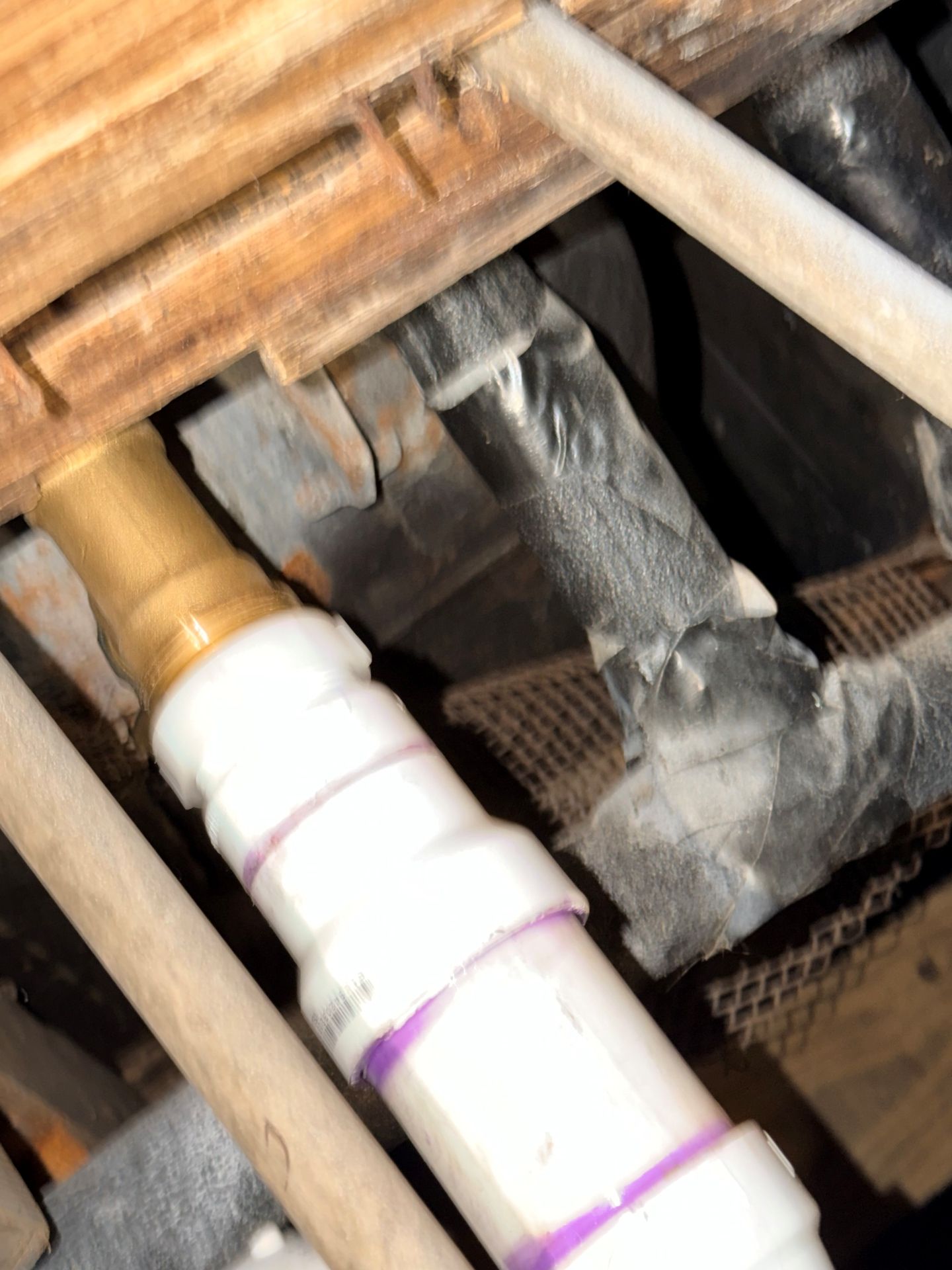 White PVC pipe with brass fitting, wrapped with purple tape, connected to a metal structure in a dimly lit, wooden setting.