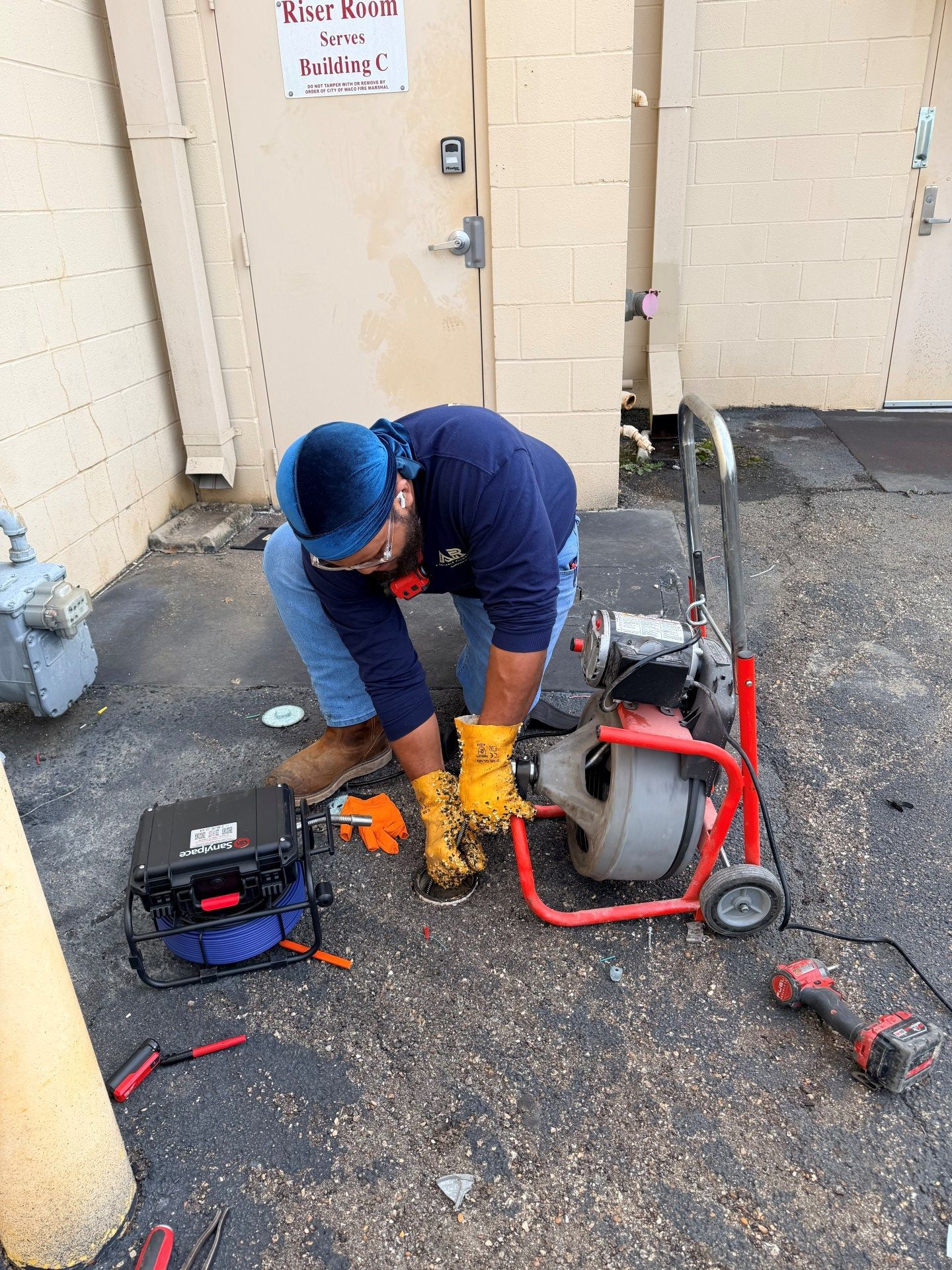 Plumber working on equipment in an outdoor setting, wearing blue and yellow protective gear.
