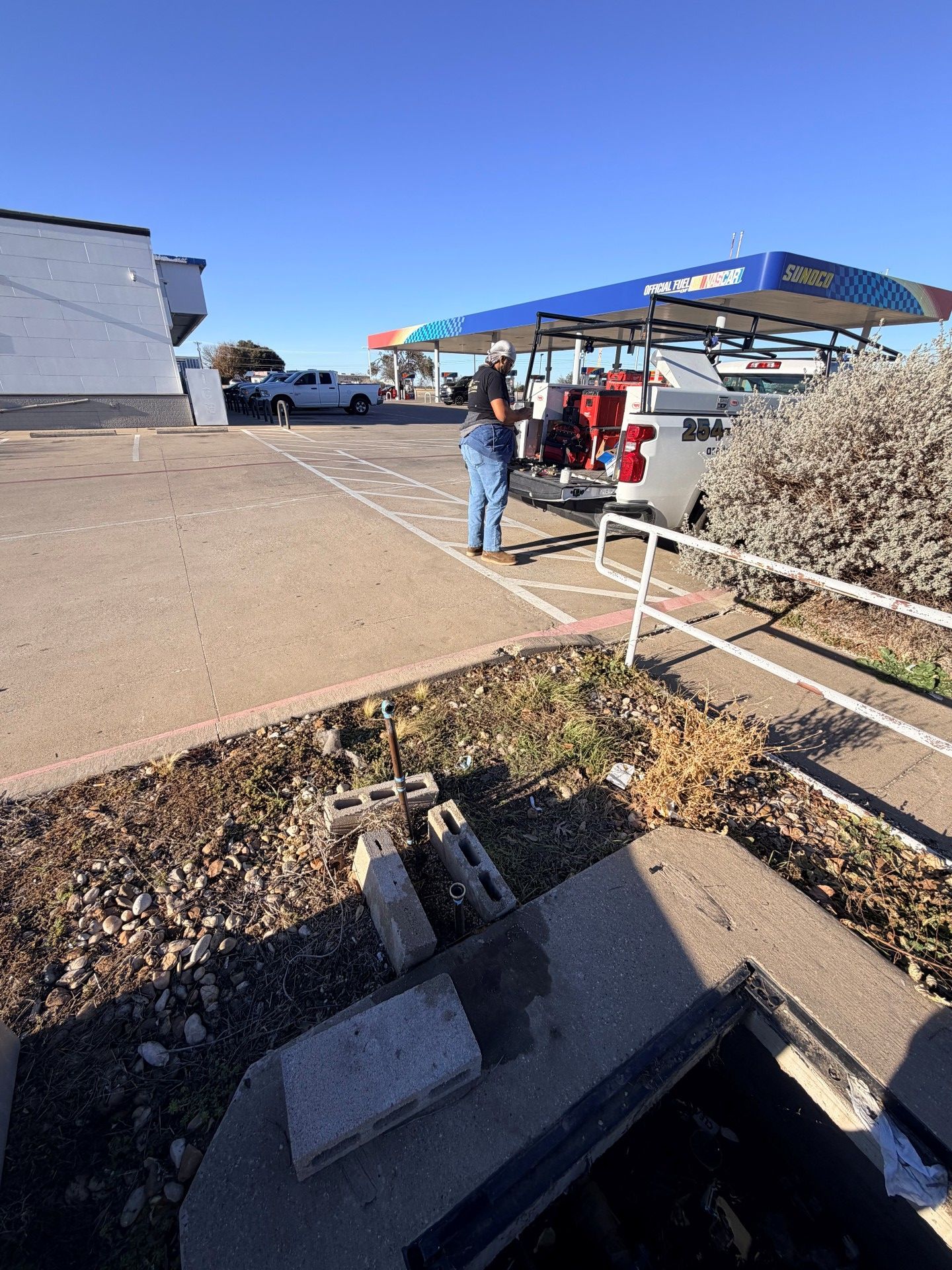 Person near a truck at a gas station. Concrete area, blue sky, and a car wash canopy in the background.