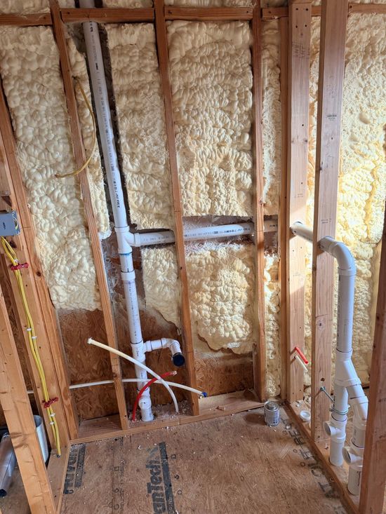 Interior of a room under construction, with exposed wooden studs, plumbing, and insulation.