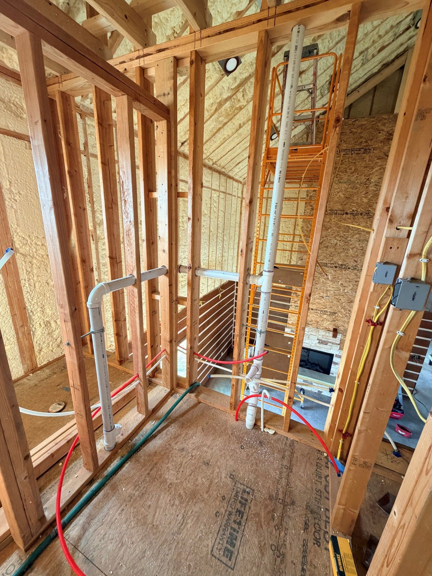 Interior construction view: wooden framing, pipes, wires, insulation, and a fireplace.