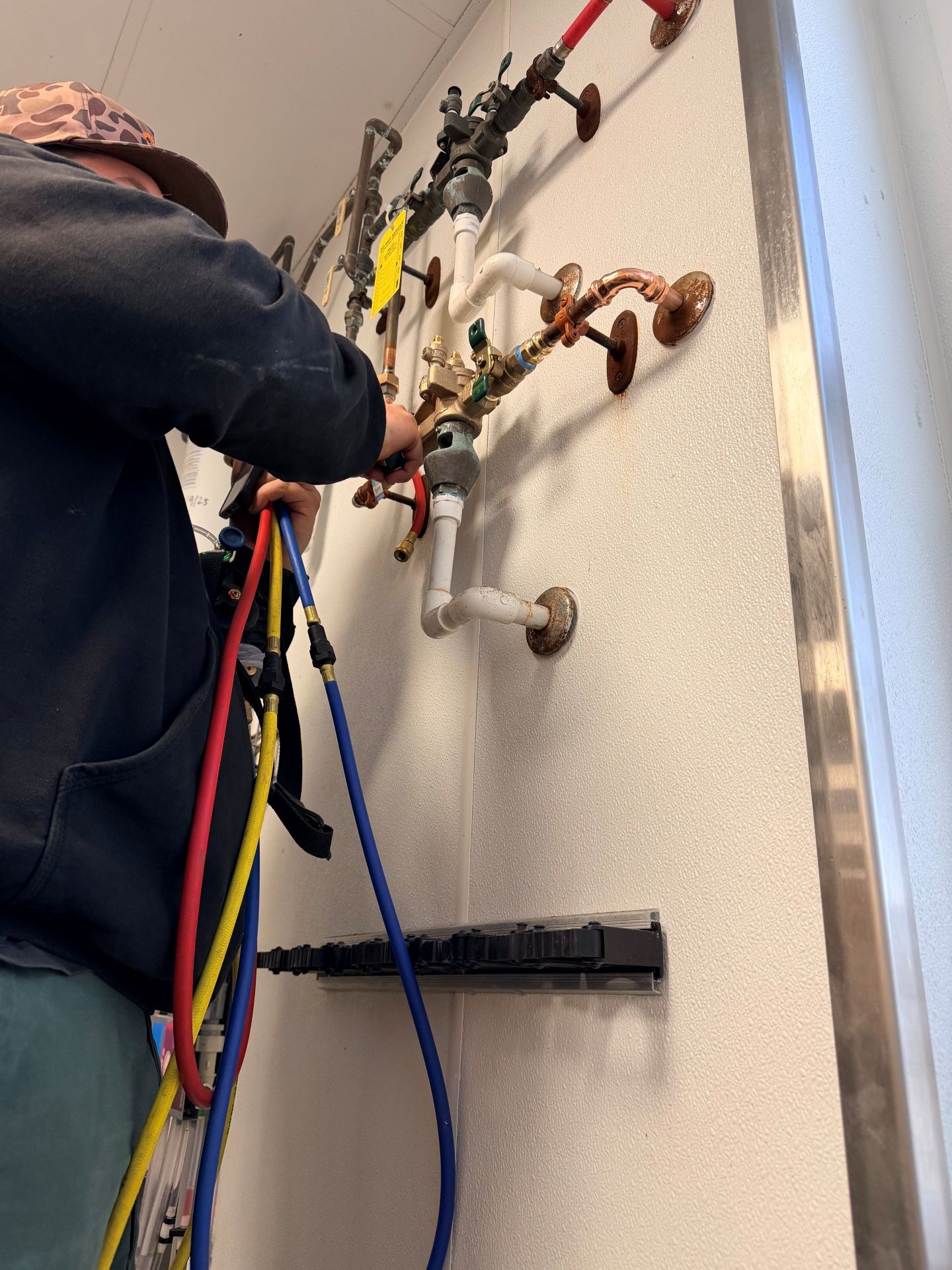 Man working on a complex network of pipes attached to a wall, holding hoses.
