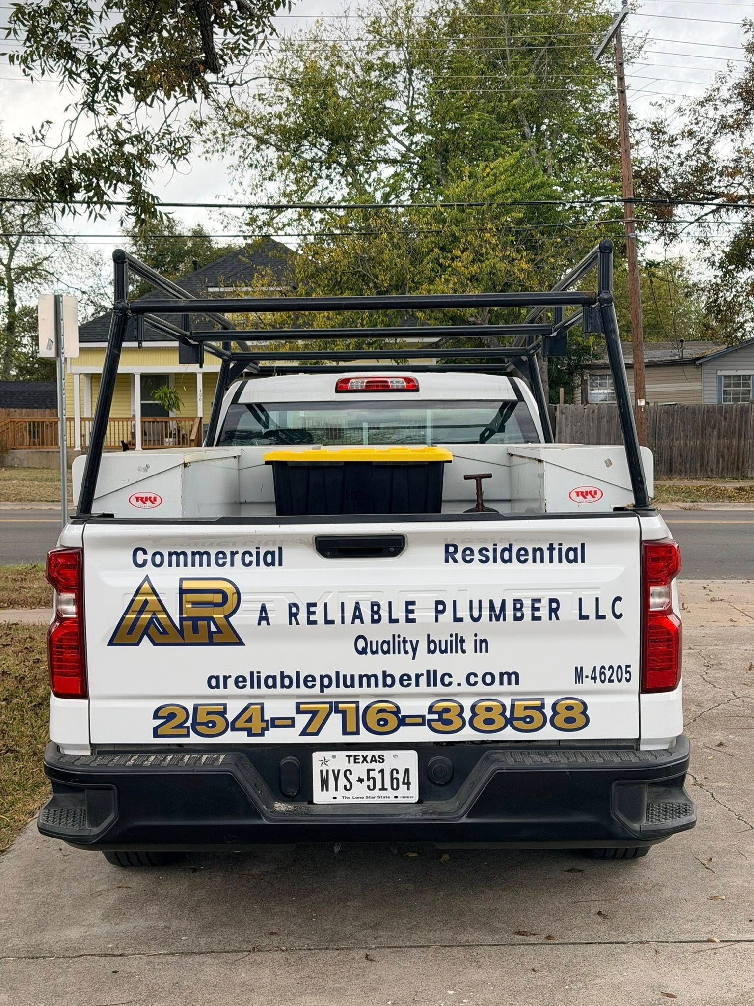 Rear view of a white plumbing truck with ladder rack. Company logo and contact info are visible.