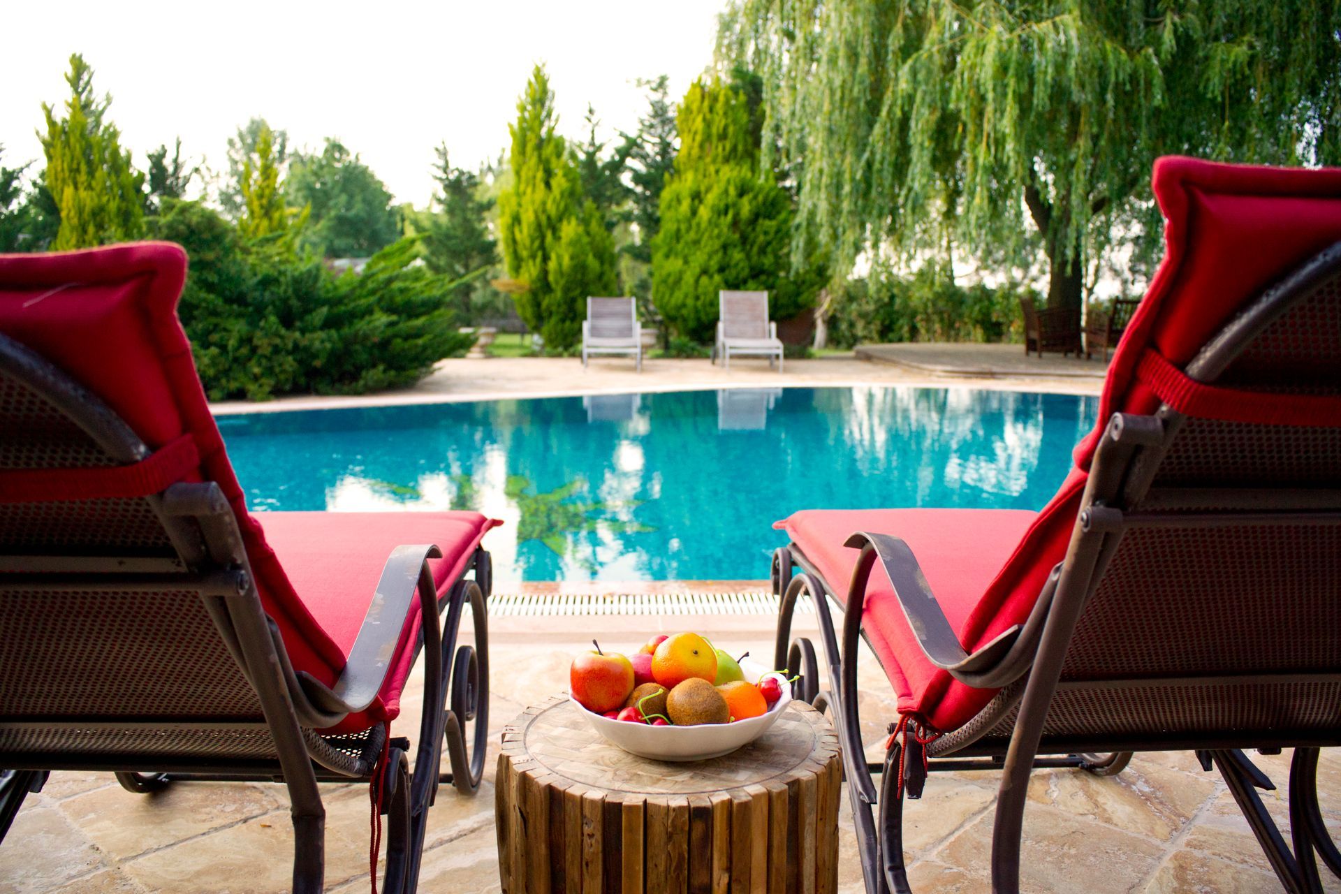 Una ciotola di frutta è appoggiata su un tavolo di legno di fronte a una piscina - International Pietre