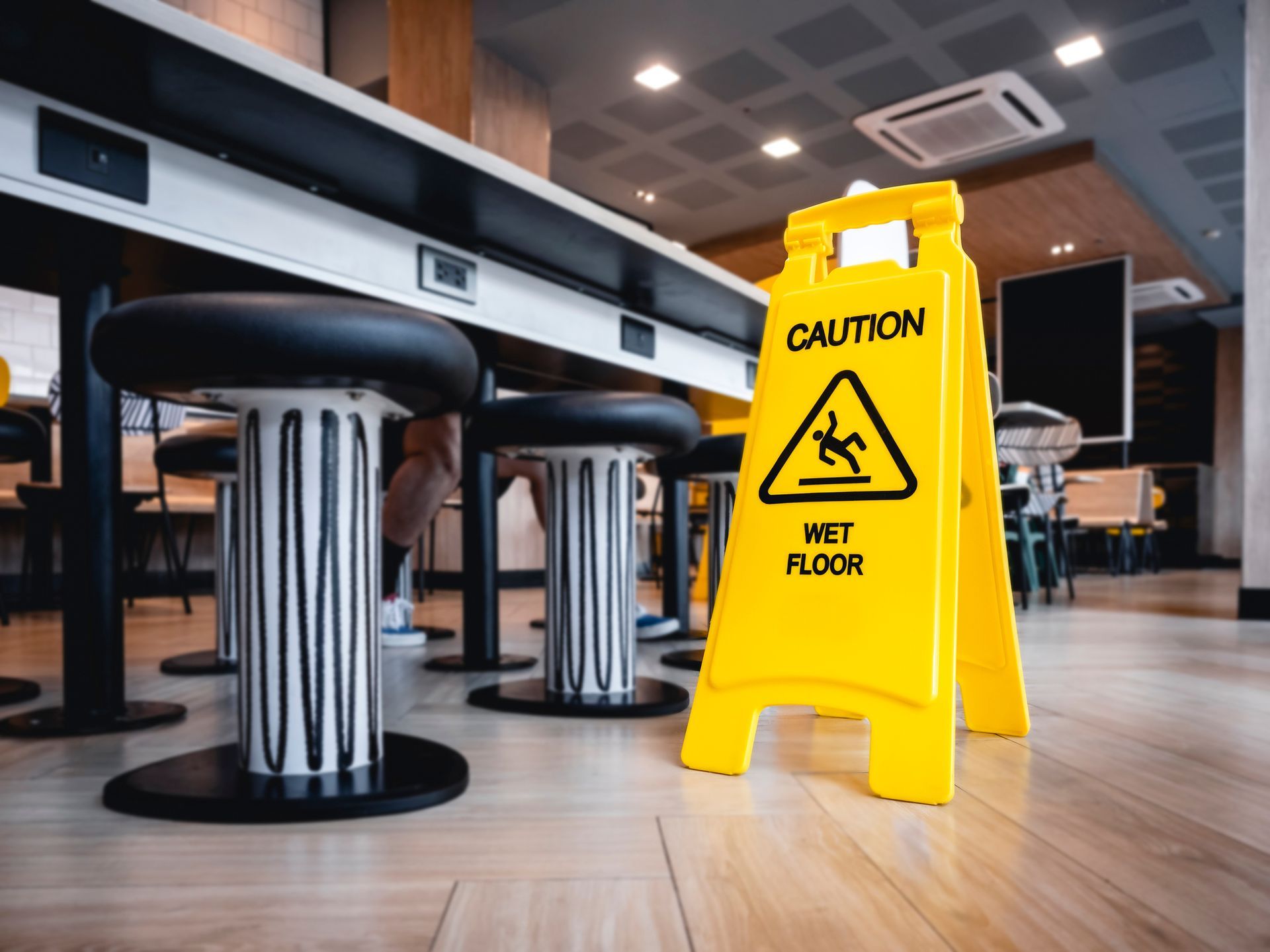 A yellow caution sign is sitting on the floor in a restaurant.