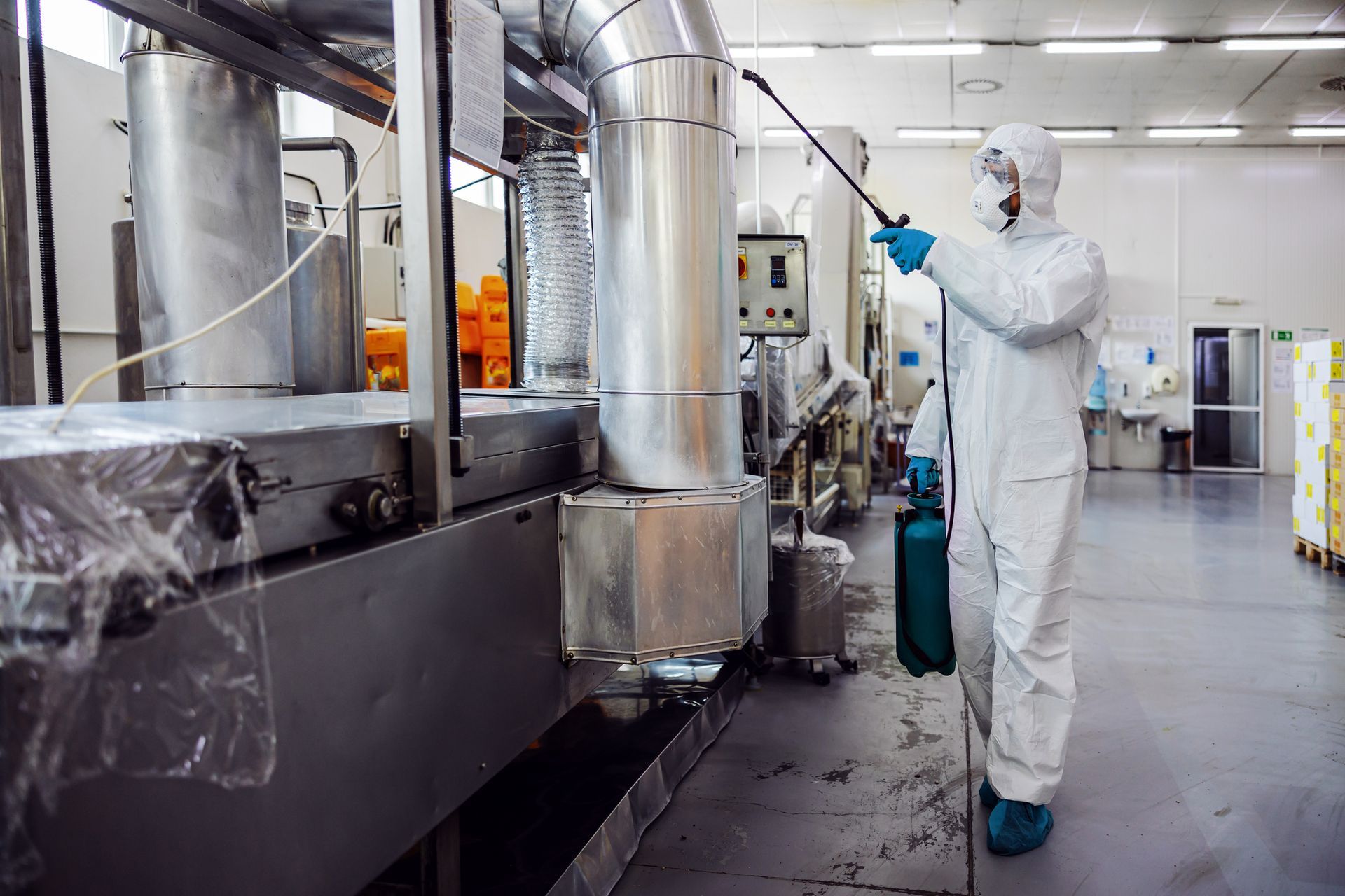 A man in a protective suit is spraying a machine in a factory.