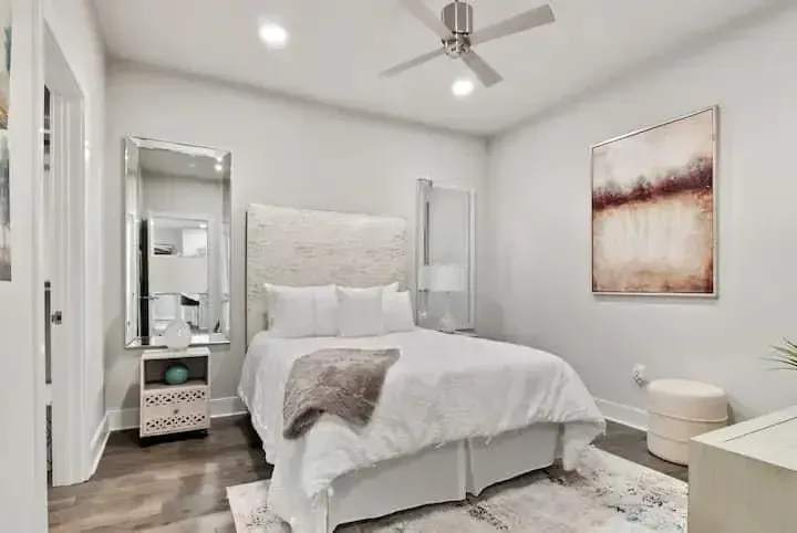 A bedroom with a bed , ceiling fan , mirror and painting on the wall.