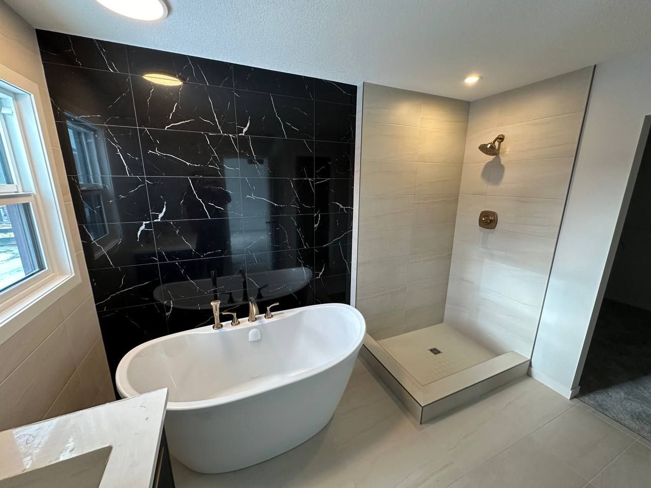 Luxurious Sherwood Park bathroom featuring a freestanding tub against black marble-look tiles and a modern shower with light
