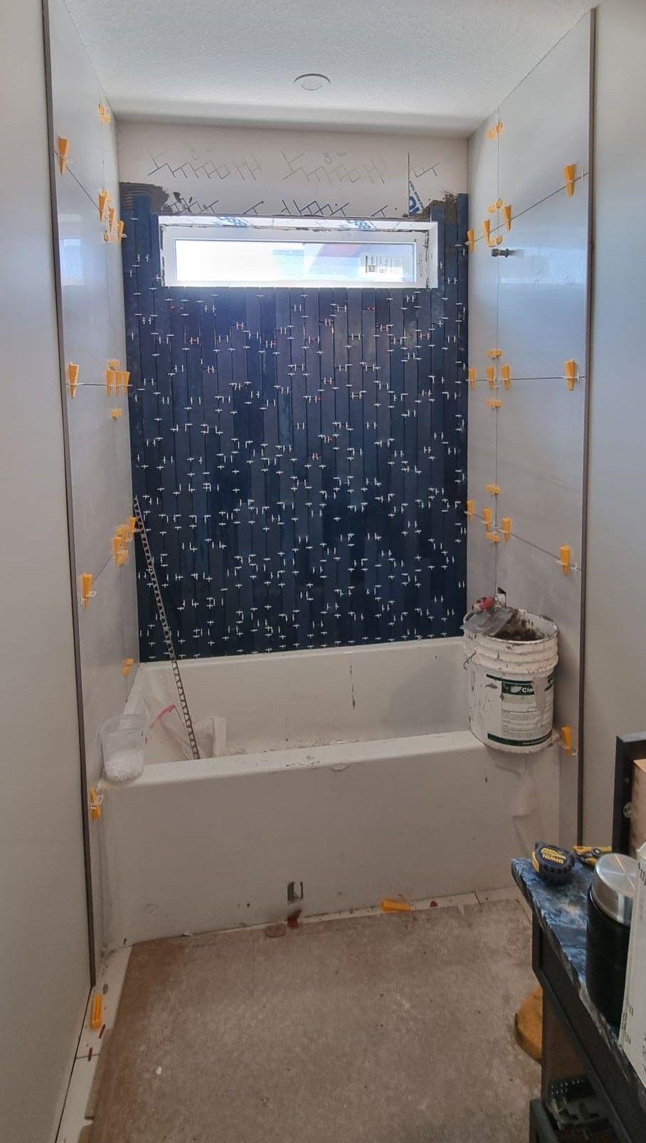 Installation of dark black vertically stacked tiles above a bathtub in a Sherwood Park bathroom by XMP Construction.