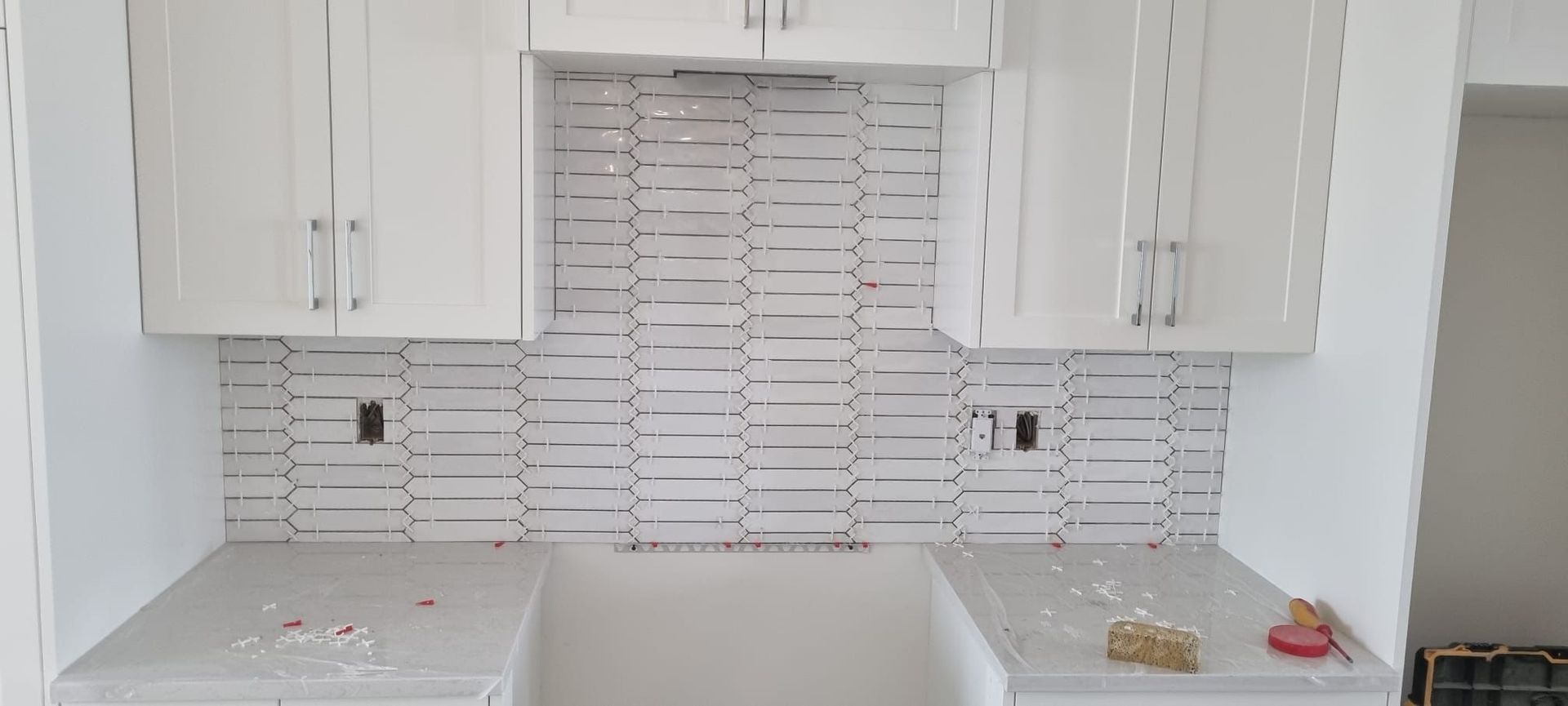Installation of unique white patterned backsplash tiles in a Sherwood Park kitchen with white cabinets by XMP Construction.