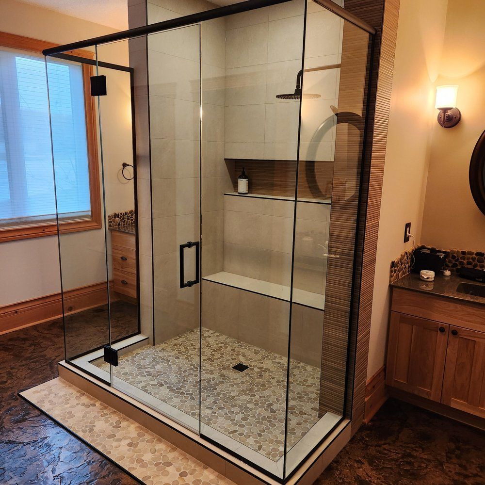 Modern glass shower enclosure with pebble floor in a Sherwood Park bathroom by XMP Construction.