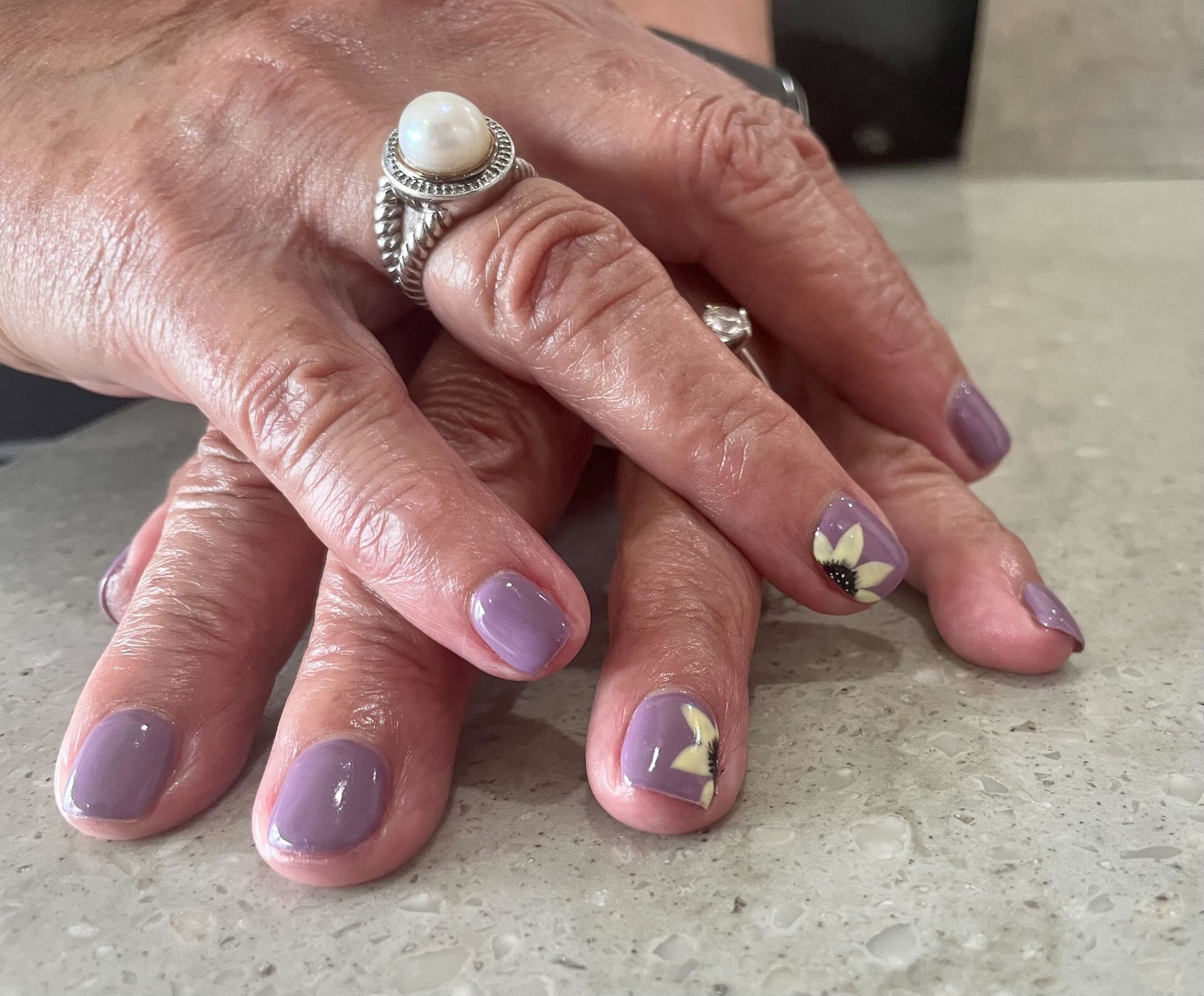 a woman 's hands with purple nails and a pearl ring
