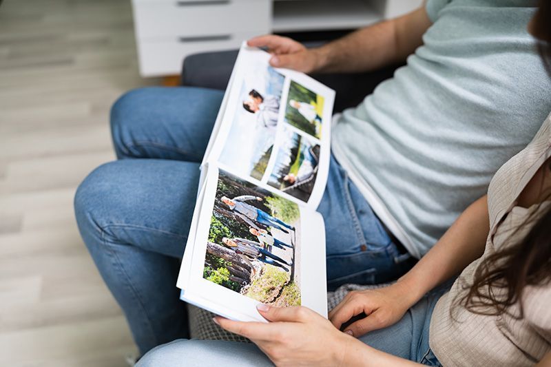 Two people sitting together, looking through a photo album with pictures of a group outdoors.