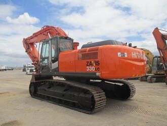 A large orange excavator is parked in a dirt lot.