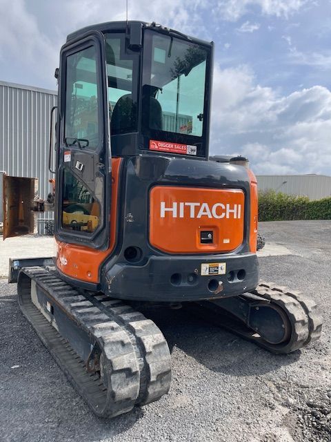 Orange Hitachi mini excavator parked on gravel outdoors, viewed from the rear-left side.
