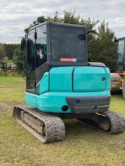 Turquoise and black tracked excavator parked on grass outdoors
