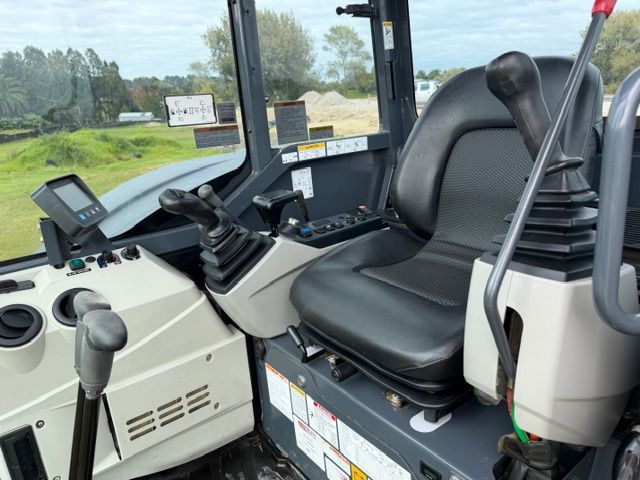 Cab of a construction vehicle with black seat, controls, and window view of a roadside field
