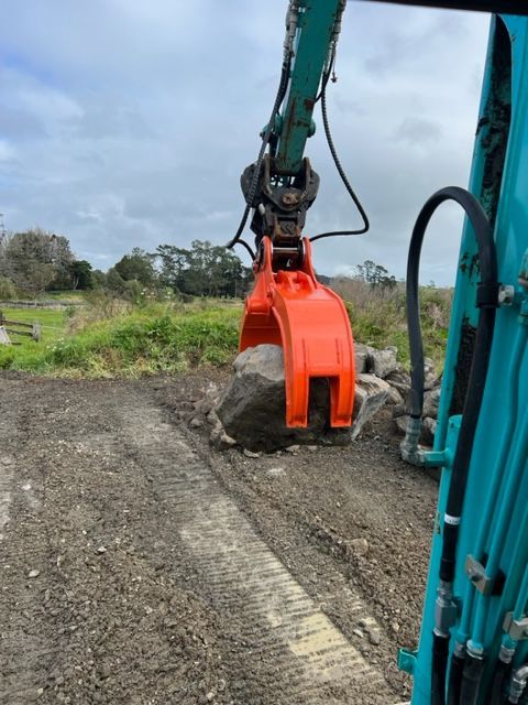 A large rock is being lifted by a crane on a dirt road.