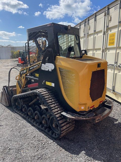 A yellow and black bulldozer is parked in a gravel lot next to a white container.