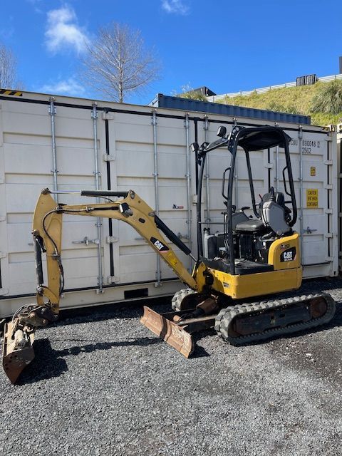 Yellow mini excavator with bucket attachment parked beside a white shipping container outdoors