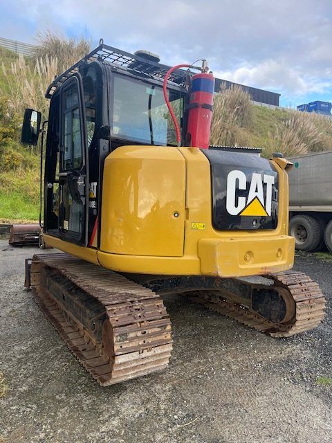 A yellow cat excavator is parked in a gravel lot next to a truck.