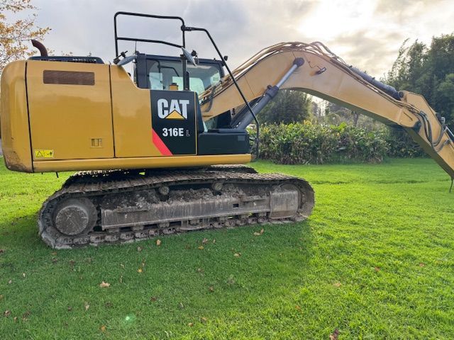 A cat excavator is parked in a grassy field