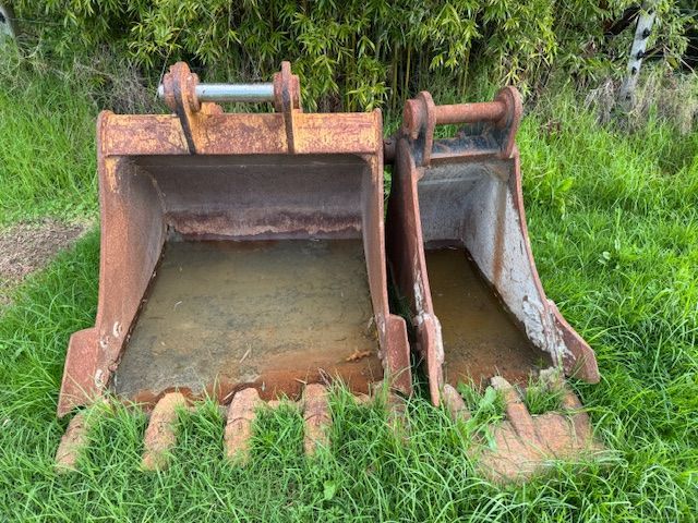 Two rusty buckets are sitting on top of a lush green field.