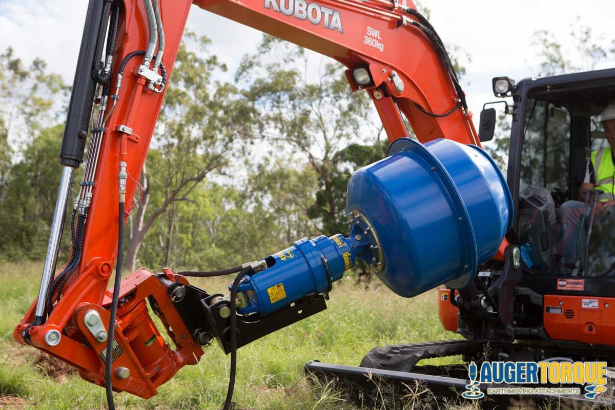A man is driving a kubota excavator with a blue barrel attached to it.