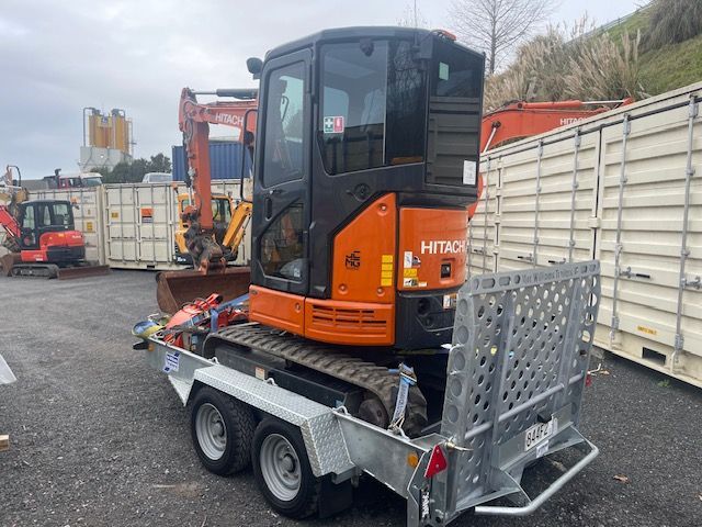 A small excavator is sitting on a trailer in a parking lot.