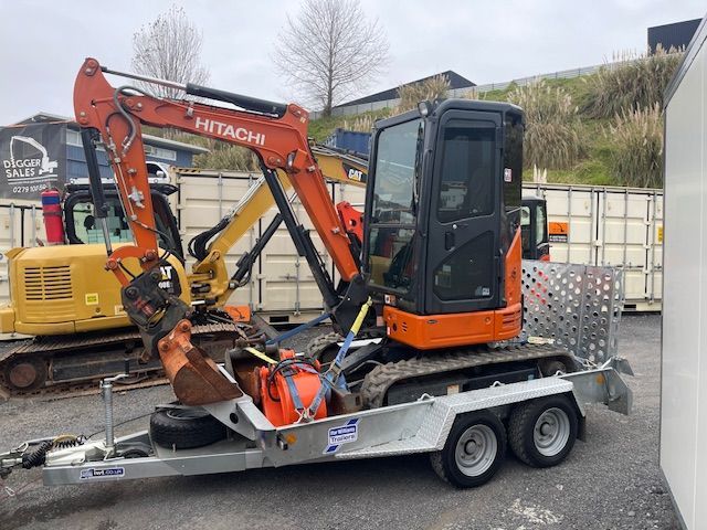 A hitachi excavator is on a trailer in a parking lot.