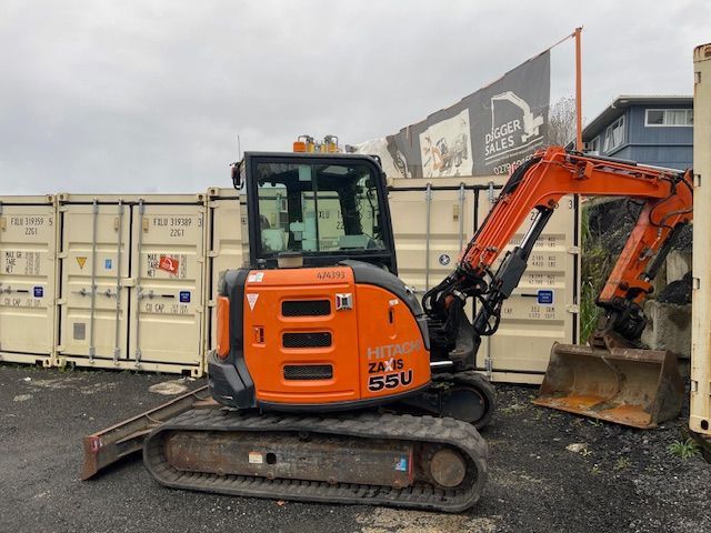 A small orange excavator is parked in front of a shipping container.