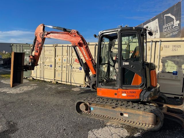 Orange mini excavator parked beside shipping containers in a gravel yard