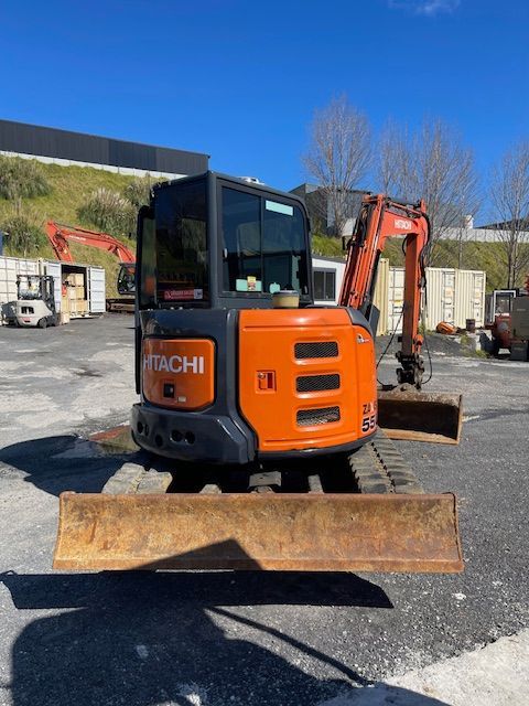 Orange Hitachi mini excavator with front blade parked on gravel at a construction site.