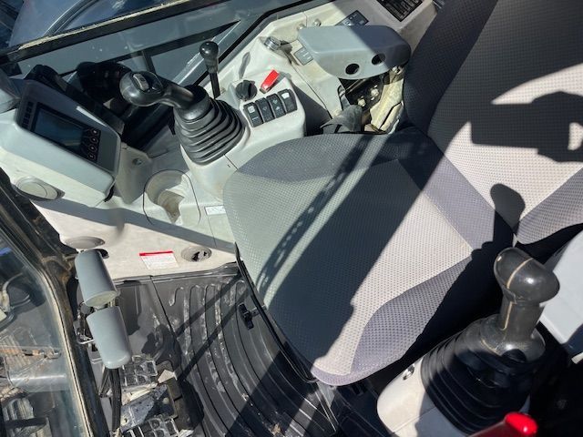 Cockpit with two joysticks, control panel, and gray patterned seat inside a vehicle or machine cab
