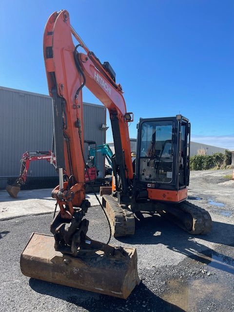 Orange excavator parked on gravel beside a metal building under a clear blue sky