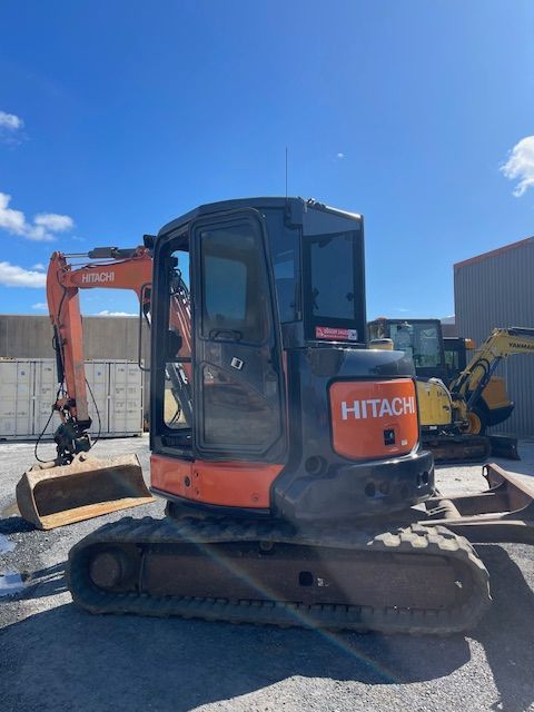 Orange Hitachi excavator parked in a construction yard under a bright blue sky.