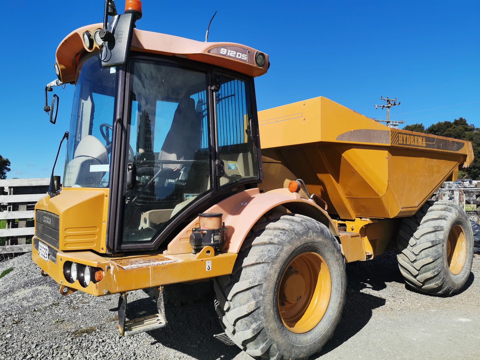 A yellow dump truck is parked in a gravel lot