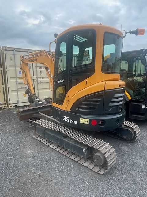 A yellow and black excavator is parked in a parking lot next to a container.