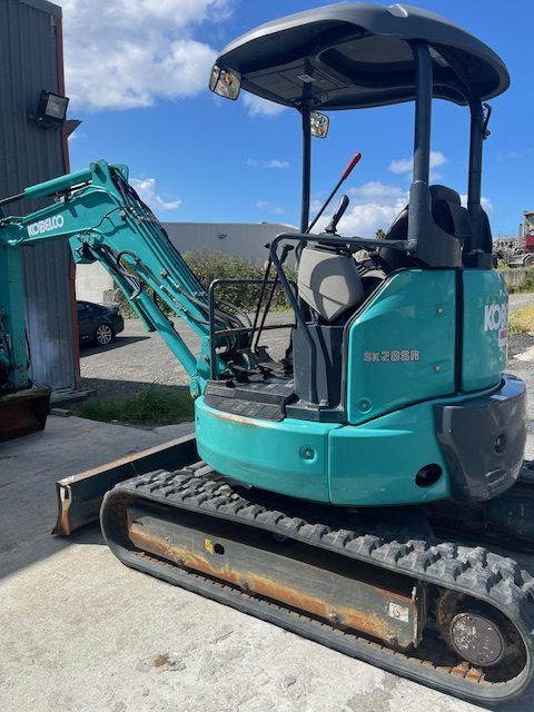 Turquoise compact excavator with tracks parked beside a building outdoors