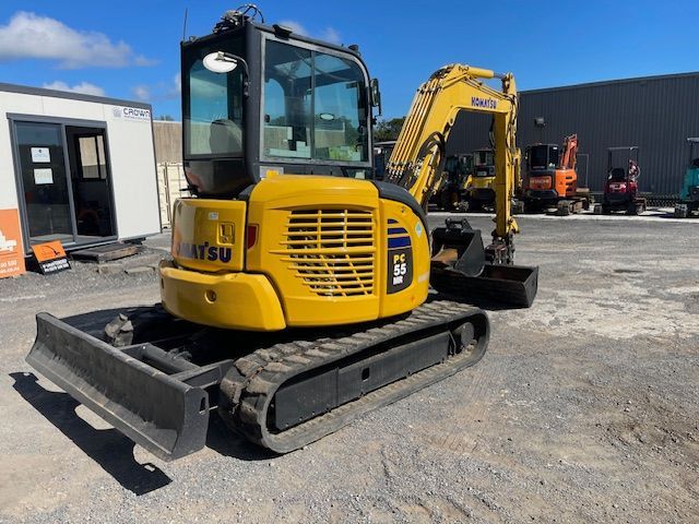 Yellow excavator on a gravel lot beside industrial buildings
