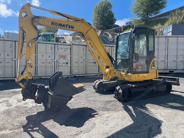 Yellow Komatsu excavator with a bucket attachment parked in a yard under a clear sky.