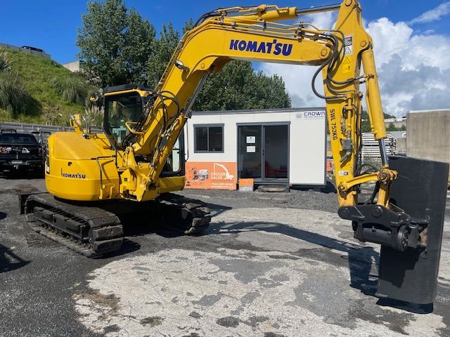 Yellow Komatsu excavator on tracks beside a small building in a gravel lot