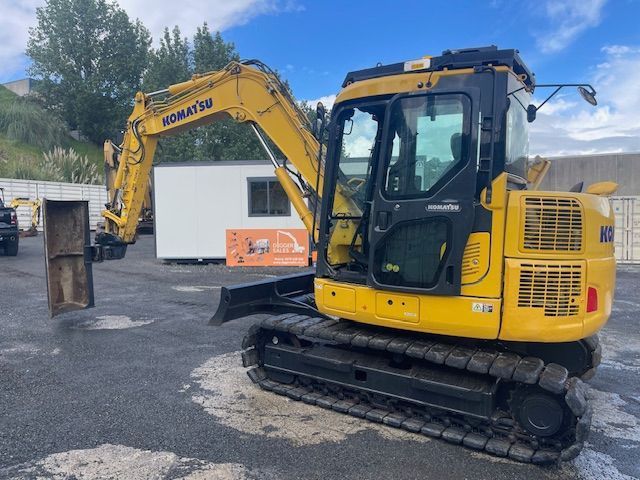 Yellow Komatsu excavator on tracks parked beside a white building at a construction site.