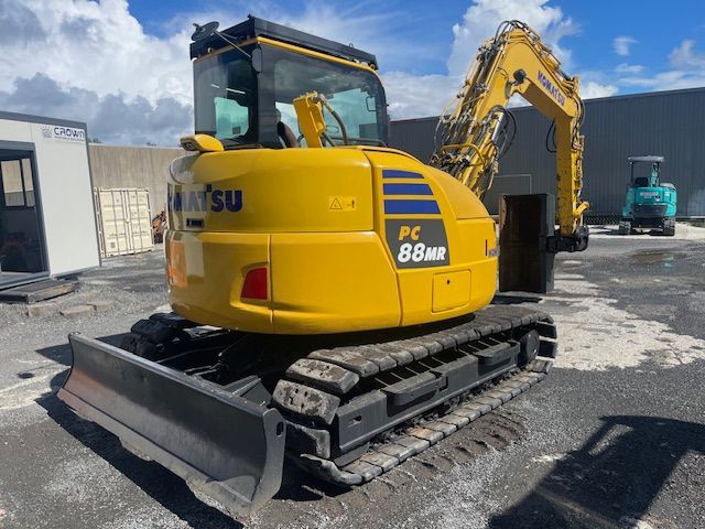 Yellow KOBELCO mini excavator on tracks parked in an industrial lot under a blue sky