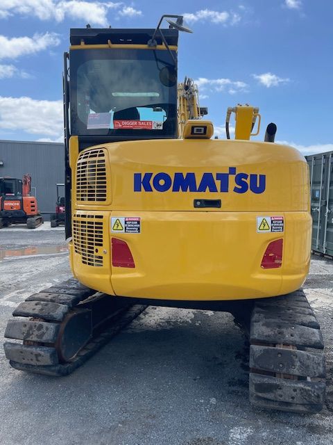 Yellow Komatsu excavator on a gravel lot under a blue sky.