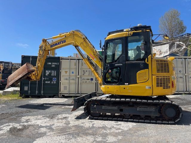 Yellow excavator on tracks unloading debris beside shipping containers in a yard