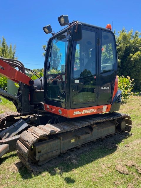 Red tracked excavator with bucket arm parked on grass under a clear blue sky.