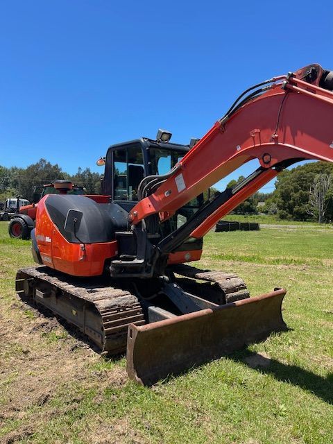 Orange and black mini excavator with blade on a grassy field under a blue sky