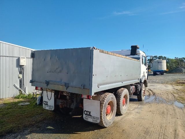 White dump truck on a dirt lot beside a metal building, viewed from the rear-left.